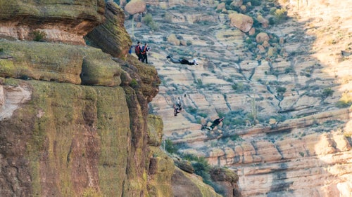 Jumpers Jordan Kilgore, Scotty Bob, and Mathew Kenney launch together in a highly coordinated jump. With three people jumping at the same time from a short cliff such as this one, jumpers must open at very specific altitudes to avoid becoming entangled in each other's parachutes.